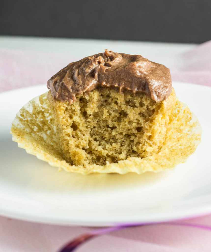 Close up side view of Vegan Whole Wheat Vanilla Cupcake with chocolate frosting and a bite taken of it. 