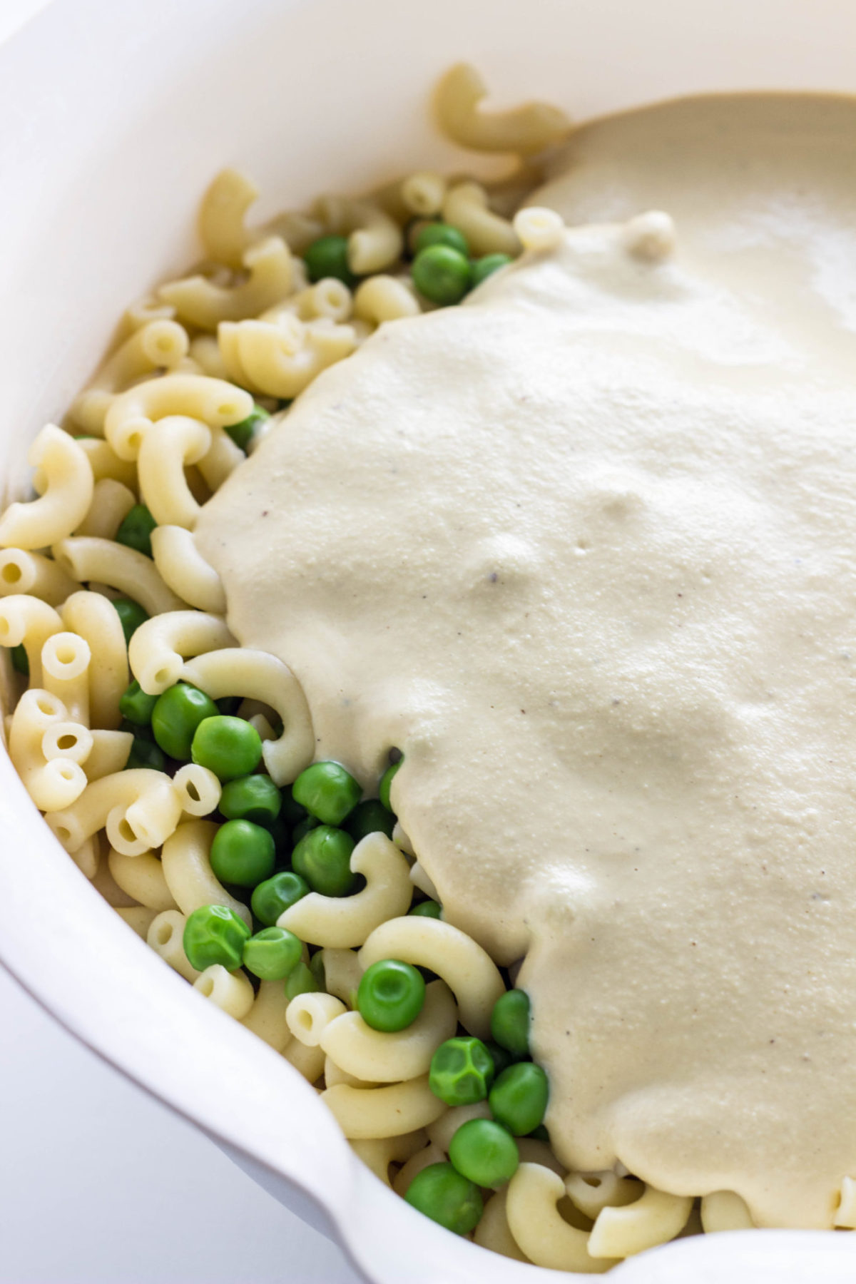 Pasta and peas in a white bowl with cashew cheese sauce poured on top. 