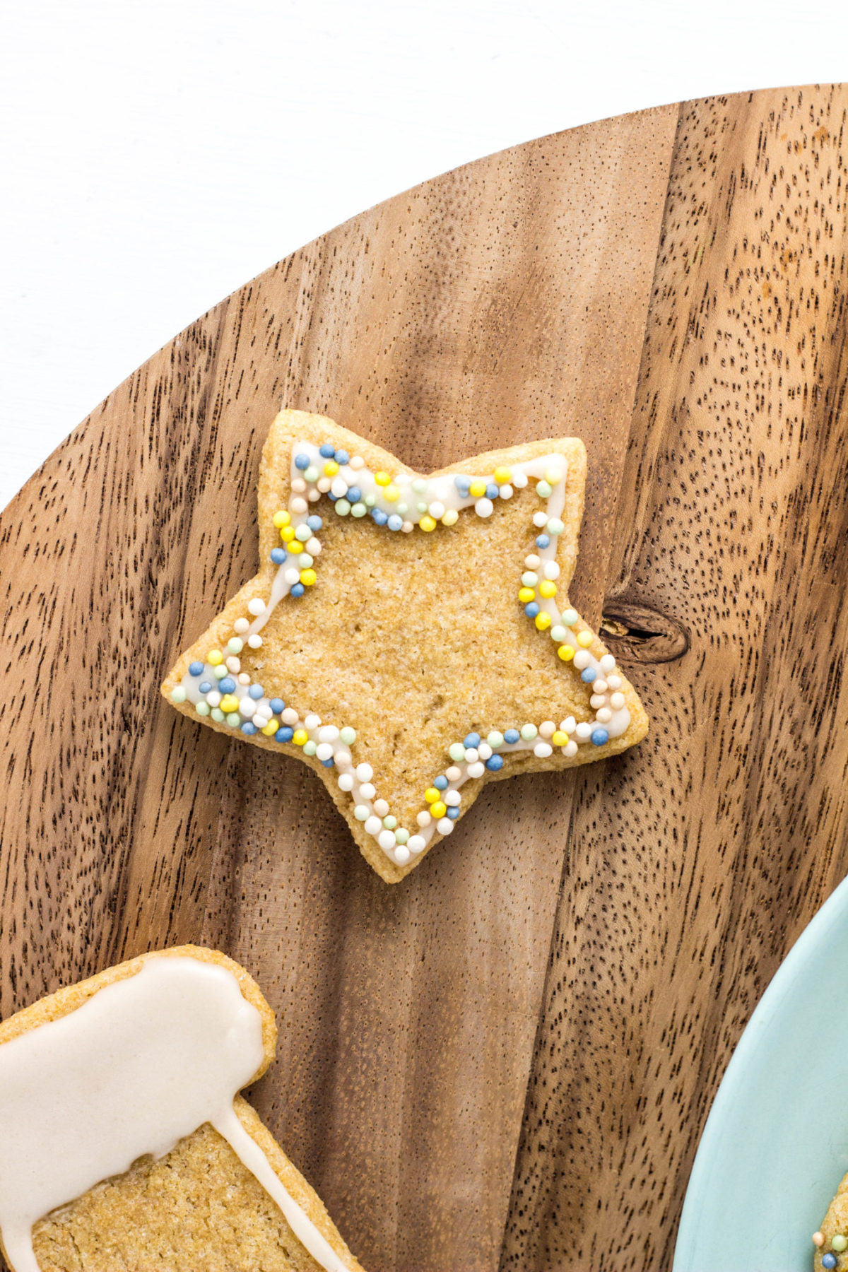 Close up top view of star shaped sugar cookie with naturally colored sprinkles around the edges on a round wooden cutting board.