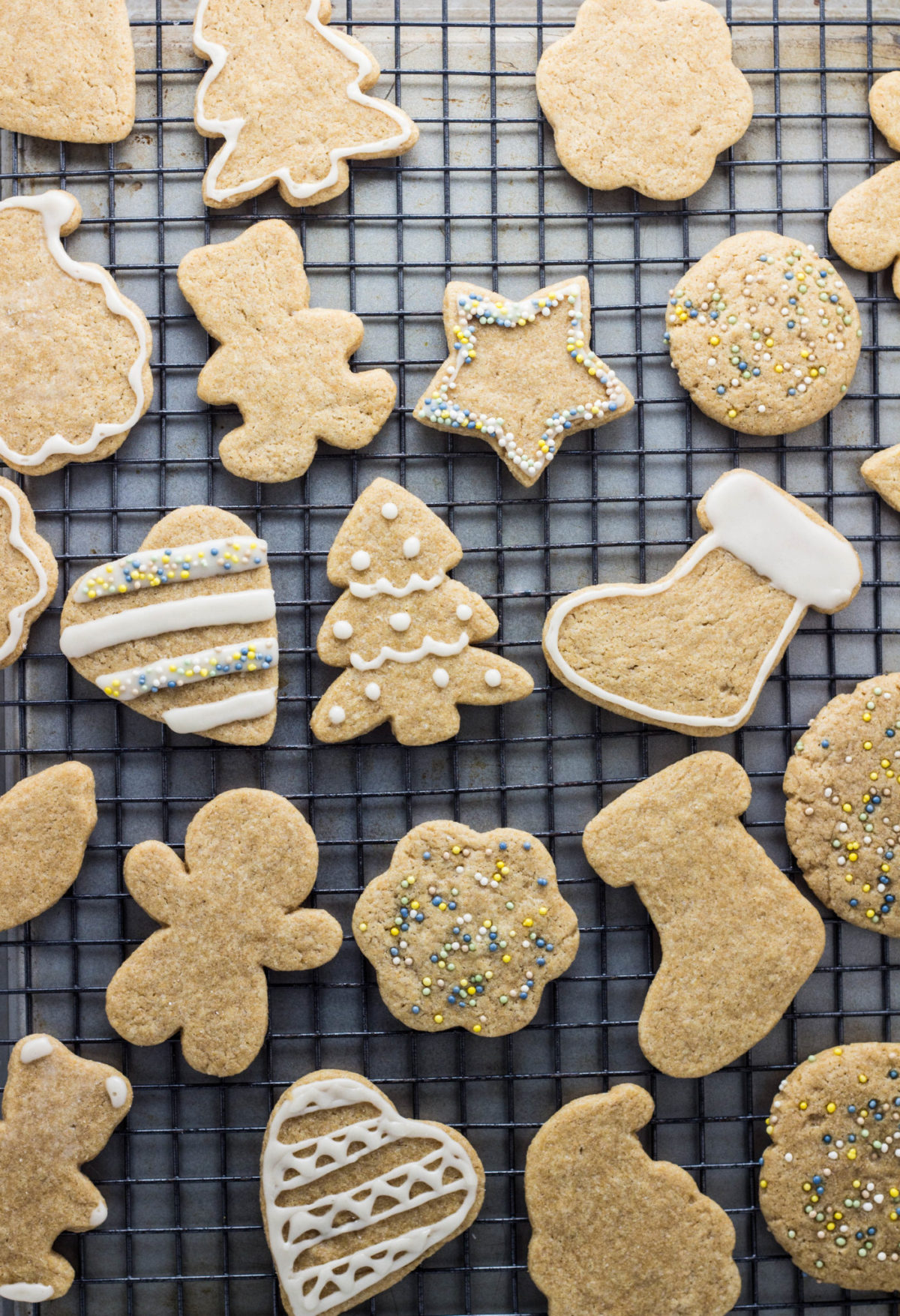 Top view of various cut out cookies on a wire cooling rack. Some are decorated with white frosting and naturally colored sprinkles. 