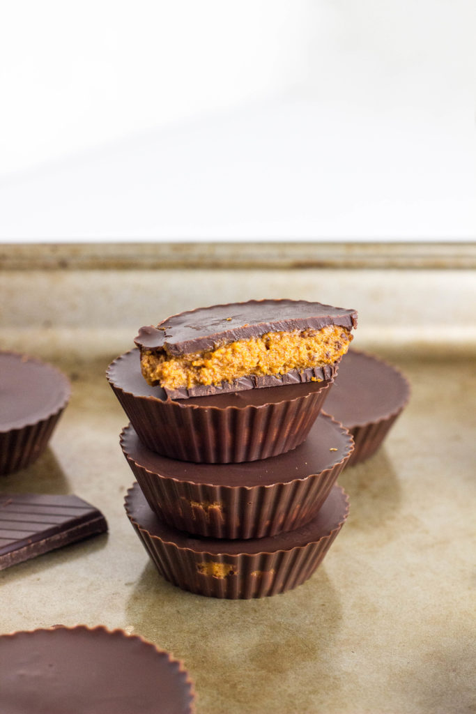Side view of a stack of Vegan Pumpkin Peanut Butter Cups. The top cup is cut in half to show the filling inside. 