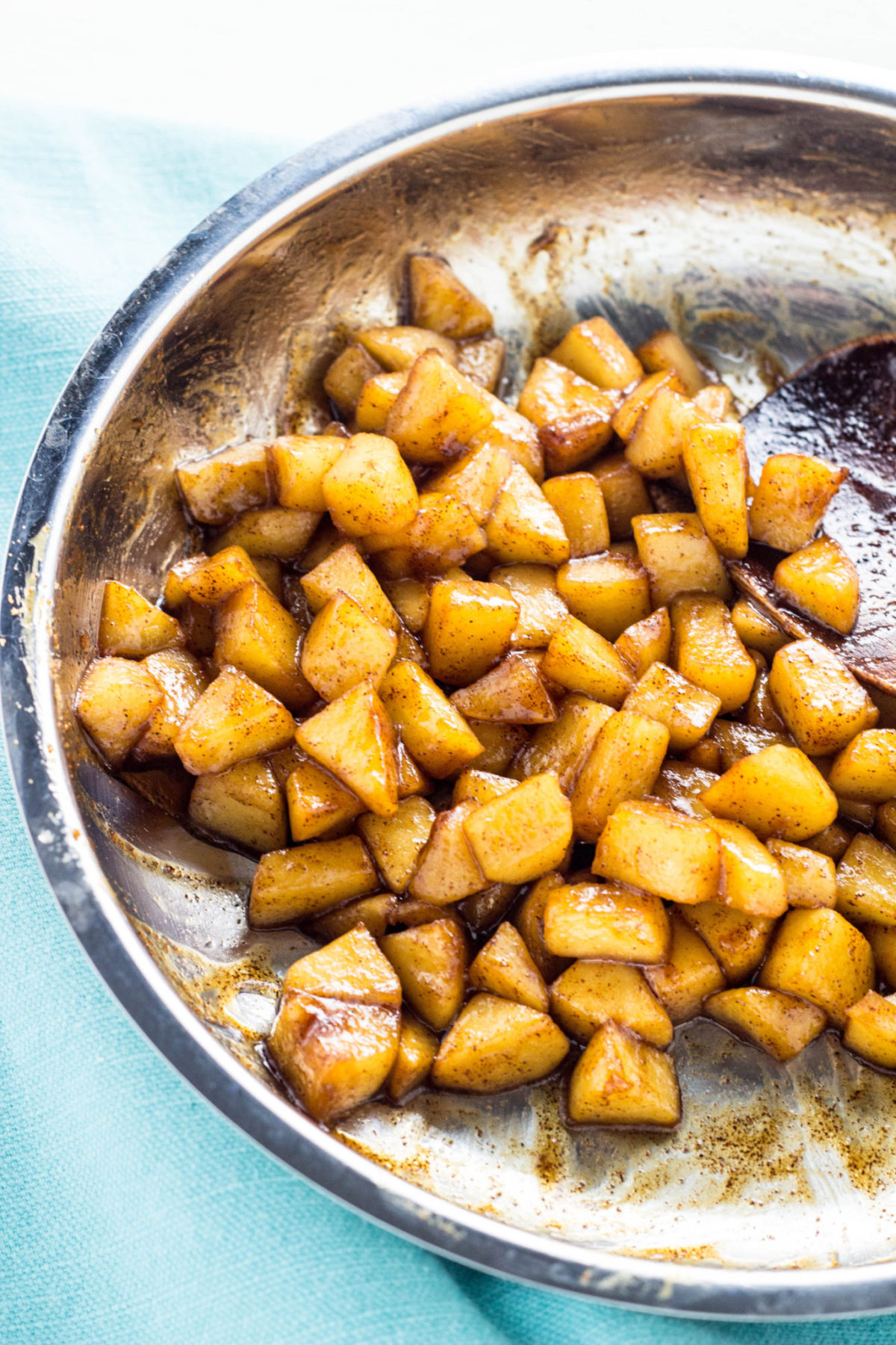 Close up of sautéed apple pieces with cinnamon in a stainless steel pan. 