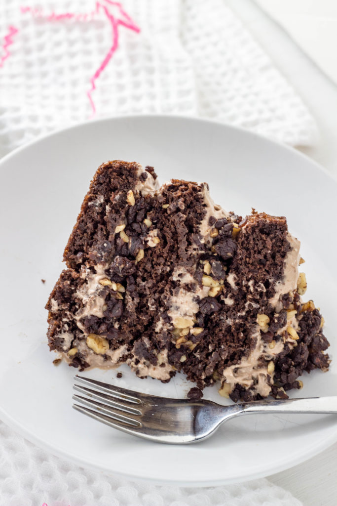 Close up side view of a slice of Vegan Chocolate Brownie Cake on a white plate with a fork. 