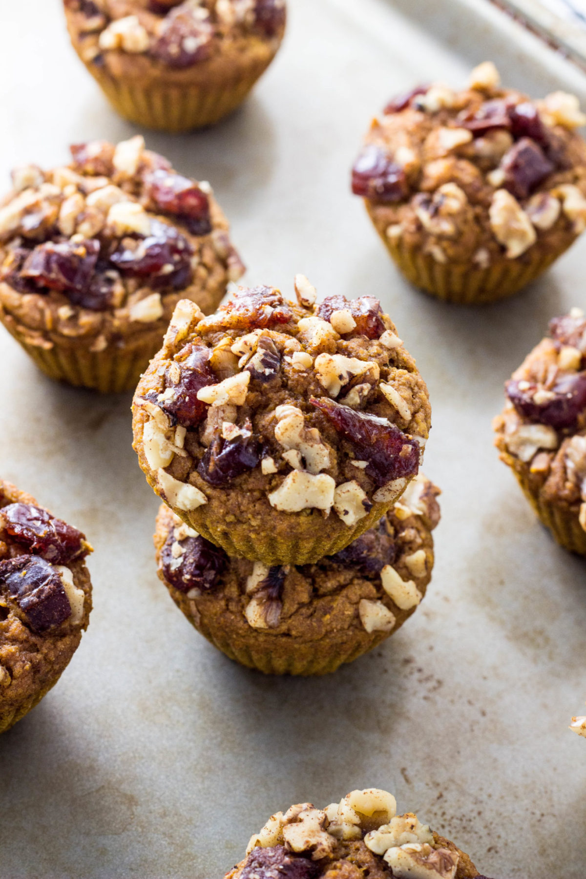 Two Vegan Date & Nut Crumble Pumpkin Muffins stacked on a baking sheet with other muffins around. 