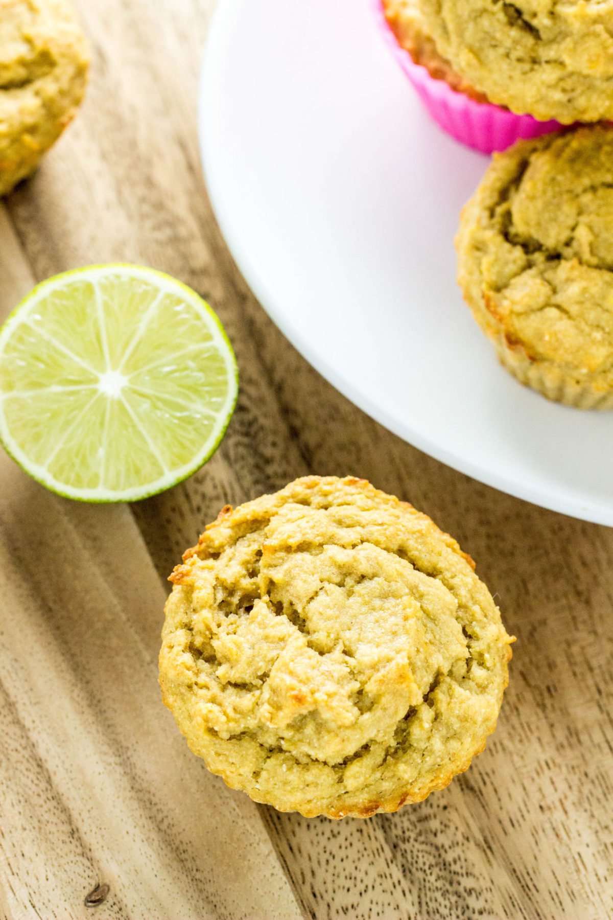 Close up top view of Vegan Lime Avocado Muffin.  A lime and part of a plate with more muffins on it is partially in frame. 