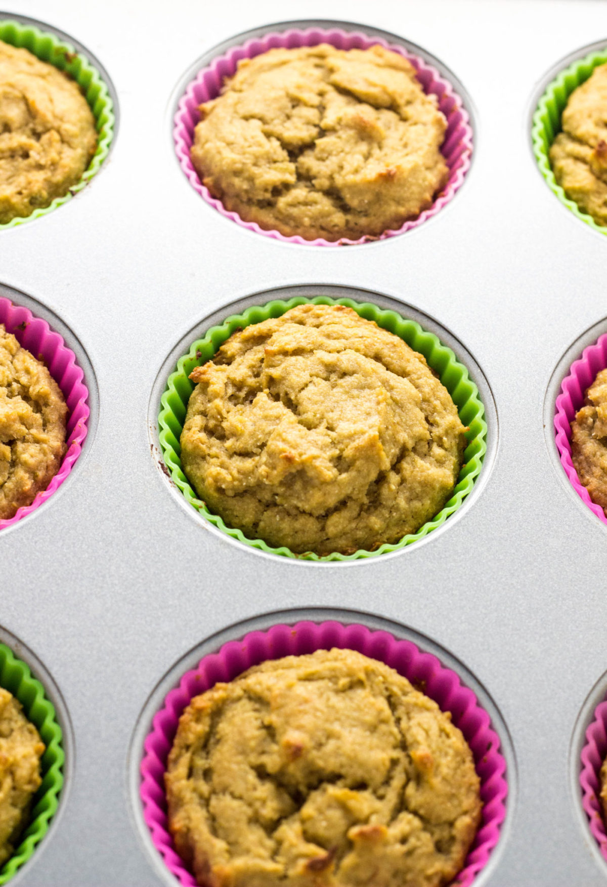 Vegan Lime Avocado Muffins in multi colored silicone baking cups cooling in a muffin pan after baking. 