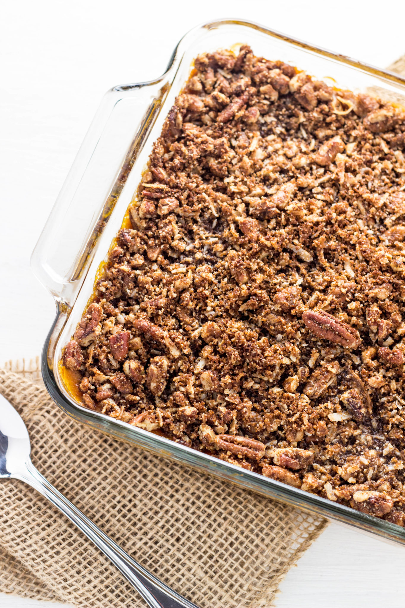 Side view of the corner of glass dish of Vegan Sweet Potato Casserole. Burlap and a spoon was partially visible to the side. 