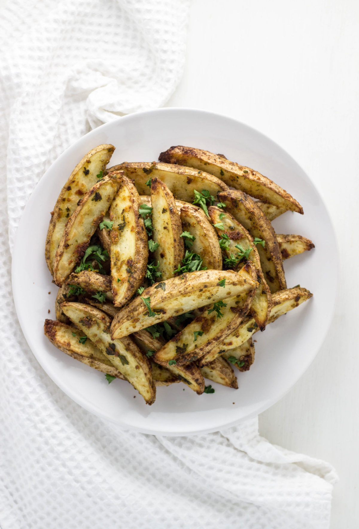 Top view of Vegan Cheesy Herb Potato Wedges on a white plate.