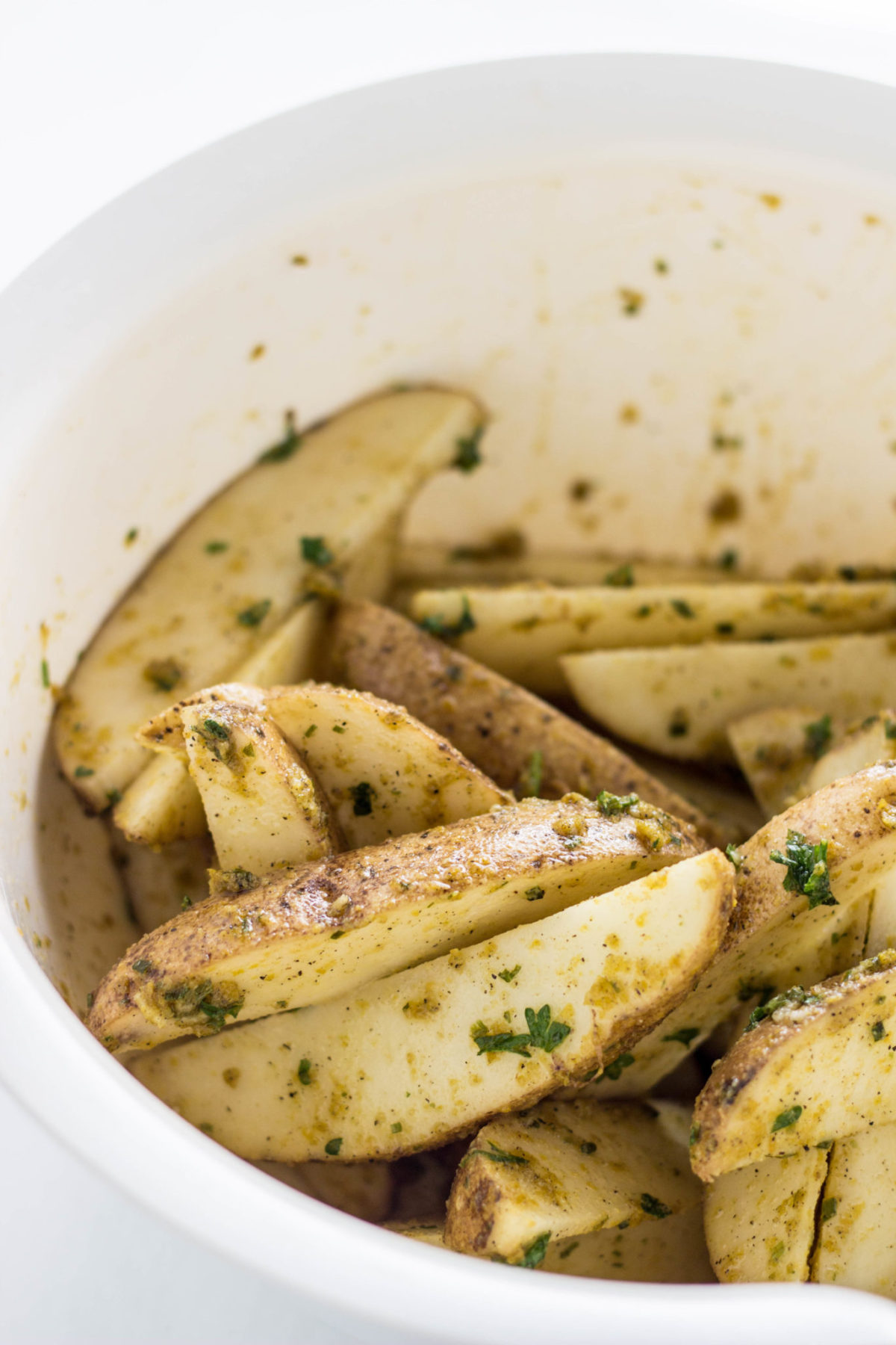 Close up of Vegan Cheesy Herb Potato Wedges in bowl before baking. 