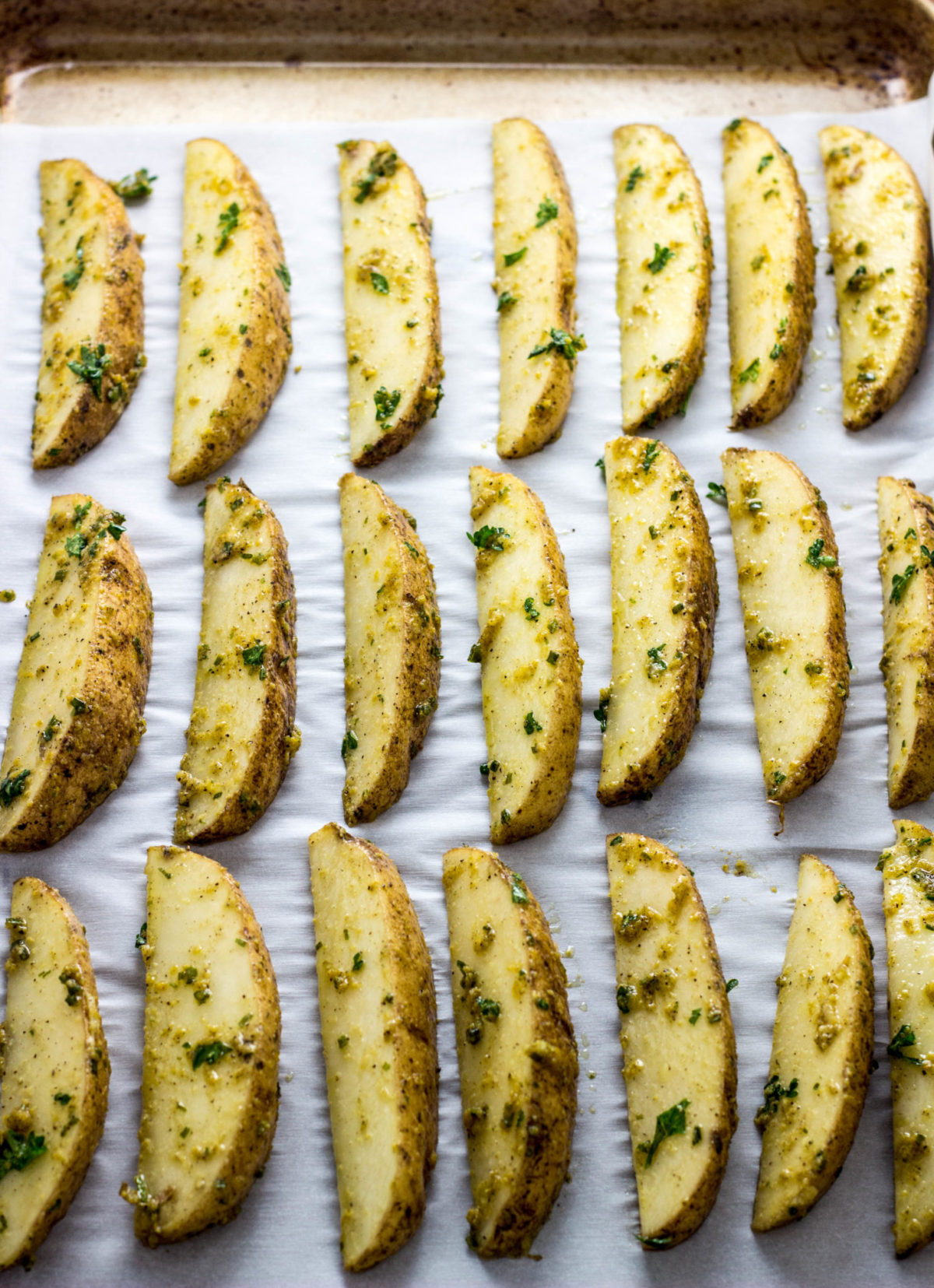 Vegan Cheesy Herb Potato Wedges arranged on baking sheet before baking.  