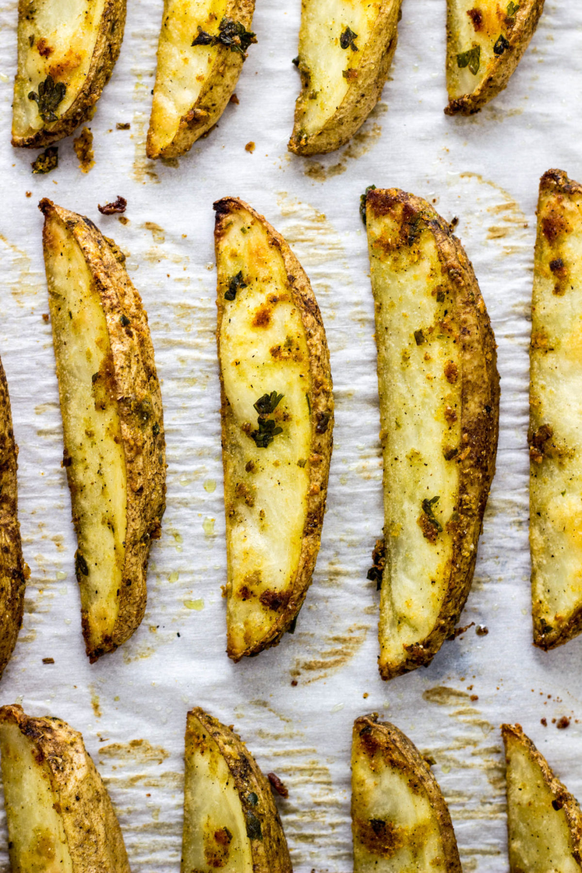 Close up of Vegan Cheesy Herb Potato Wedges on baking sheet after. baking. 