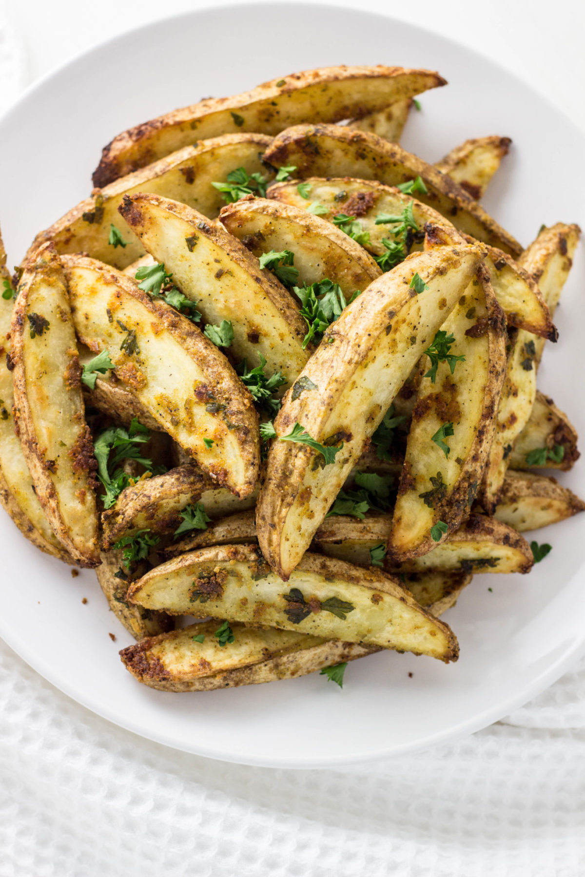 Close up of Vegan Cheesy Herb Potato Wedges on white plate. 