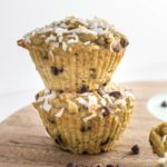 Close up side view of two Coconut Chocolate Chips Muffins stacked on a wooden cutting board.