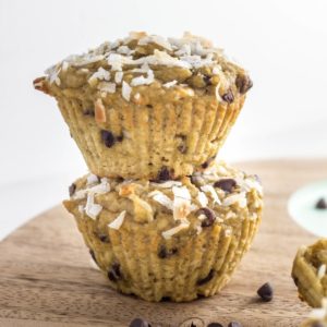 Close up side view of two Coconut Chocolate Chips Muffins stacked on a wooden cutting board.