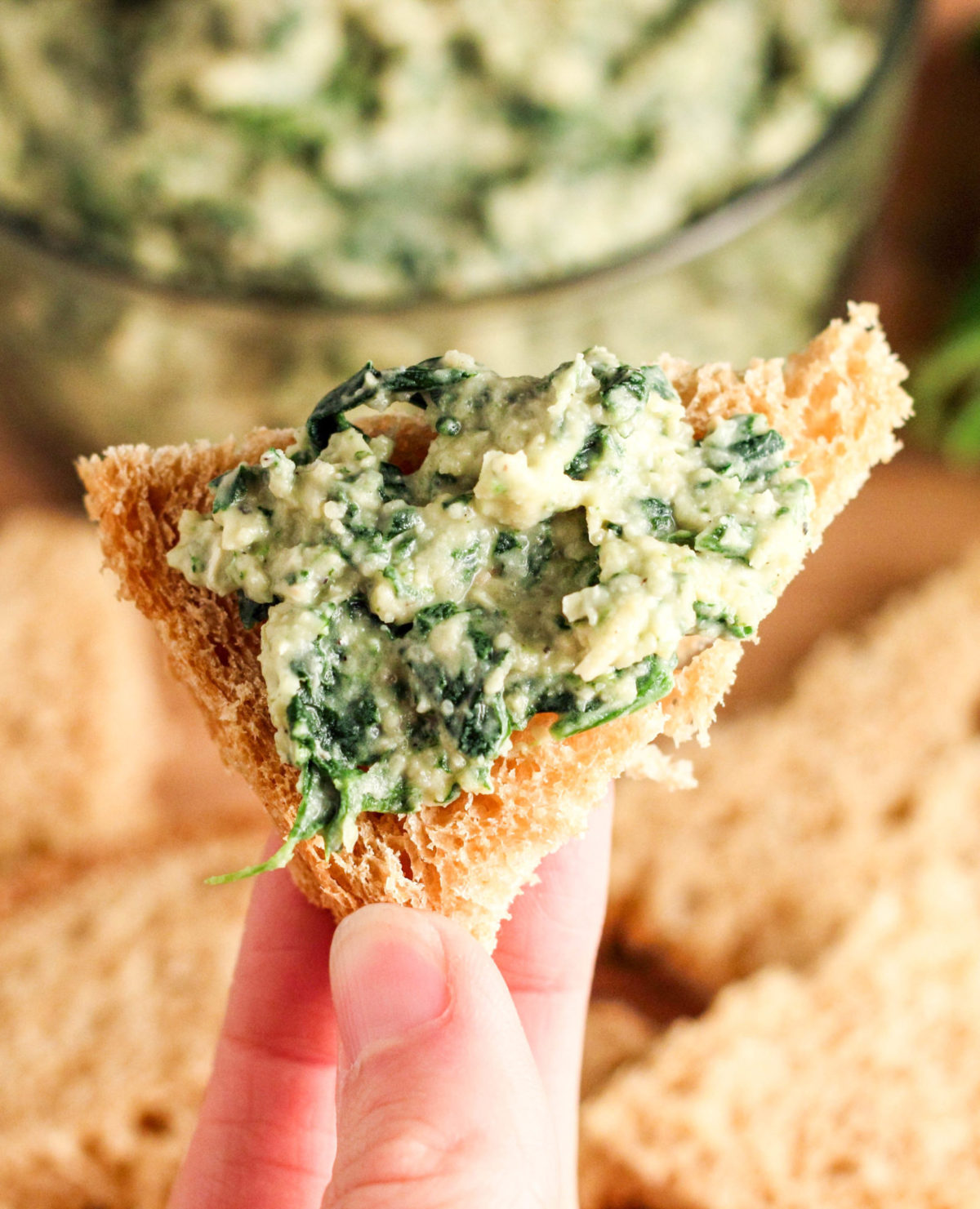 Close up top view of dip spread on bread held between fingers above a board with other pieces of bread.