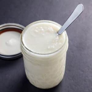 A small jar of coconut butter with a spoon sticking out of the jar on a black background.
