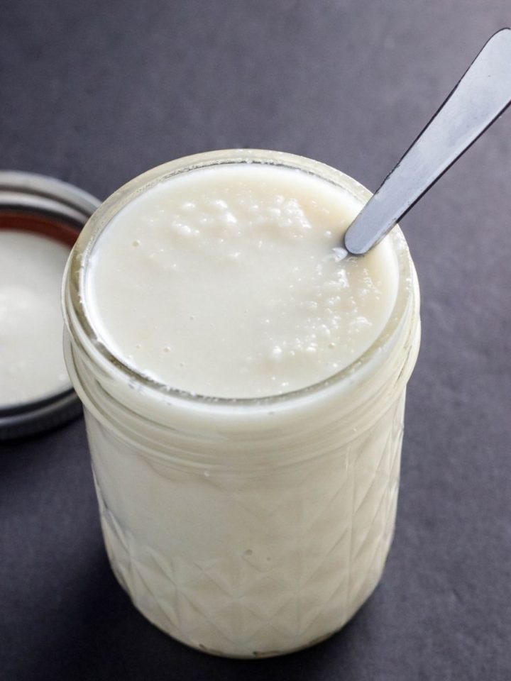 A small jar of coconut butter with a spoon sticking out of the jar on a black background.
