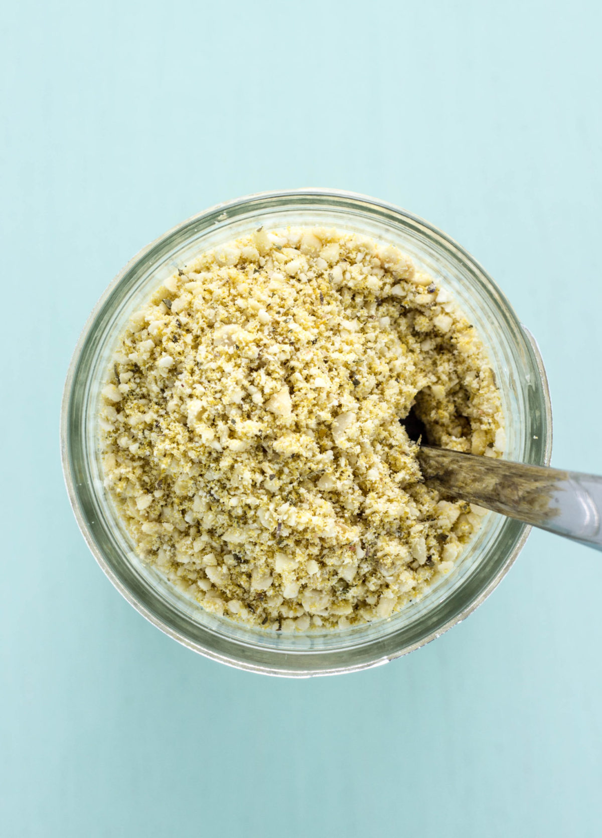 Top view of  Vegan Herbed Cashew Parmesan in a jar with a spoon. 