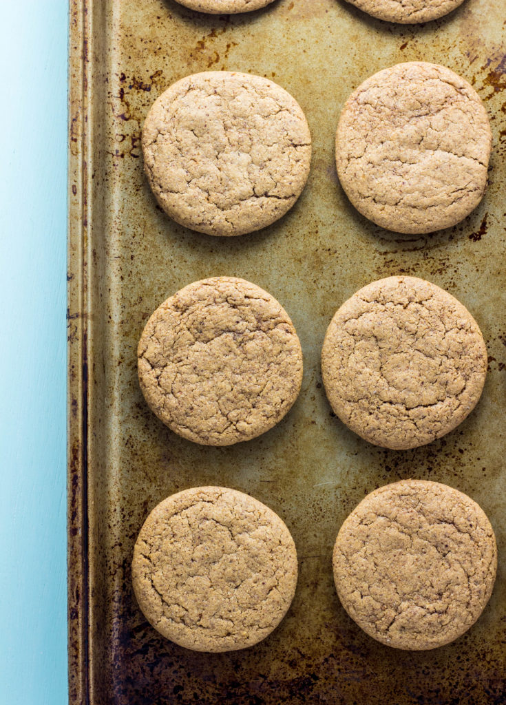 Top view of 6 Vegan Almond Butter Cookies on a baking sheet on a light blue colored background. 