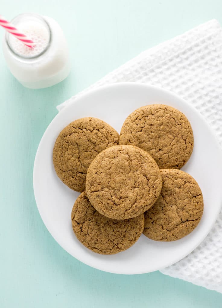 Five Vegan Almond Butter Cookies on a small white plate. A small milk bottle withe a pink and white striped straw is in the upper left corner.