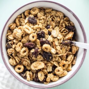 Top view close up of Oatmeal Raisin Cookie Granola in a white bowl with purple rim and a utensil handle visible on the right side.