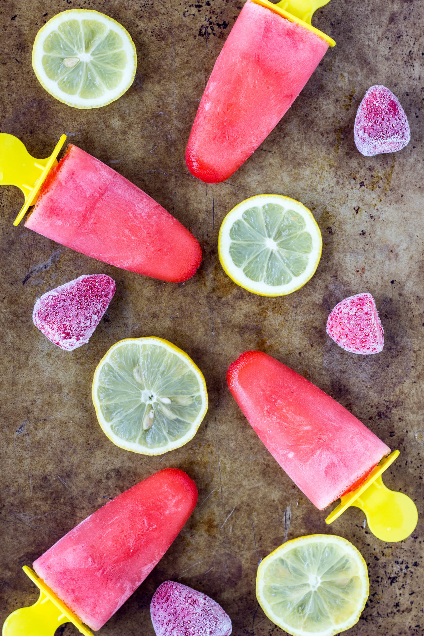 Overhead shot of Strawberry Lemonade Popsicles with slices of lemon and frozen strawberries.