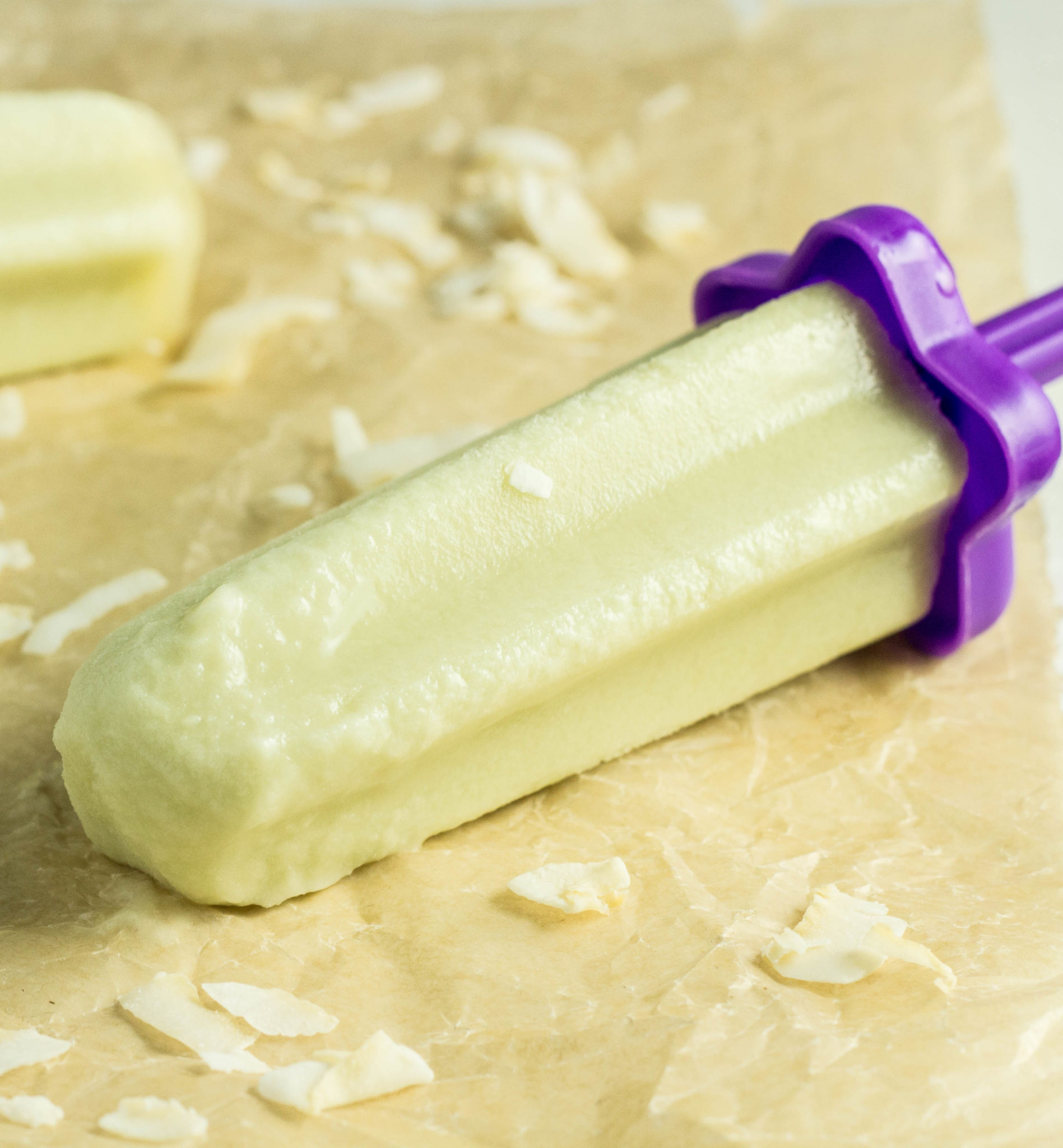 Close up of Honeydew Melon Popsicles laying on parchment paper with coconut flakes. 