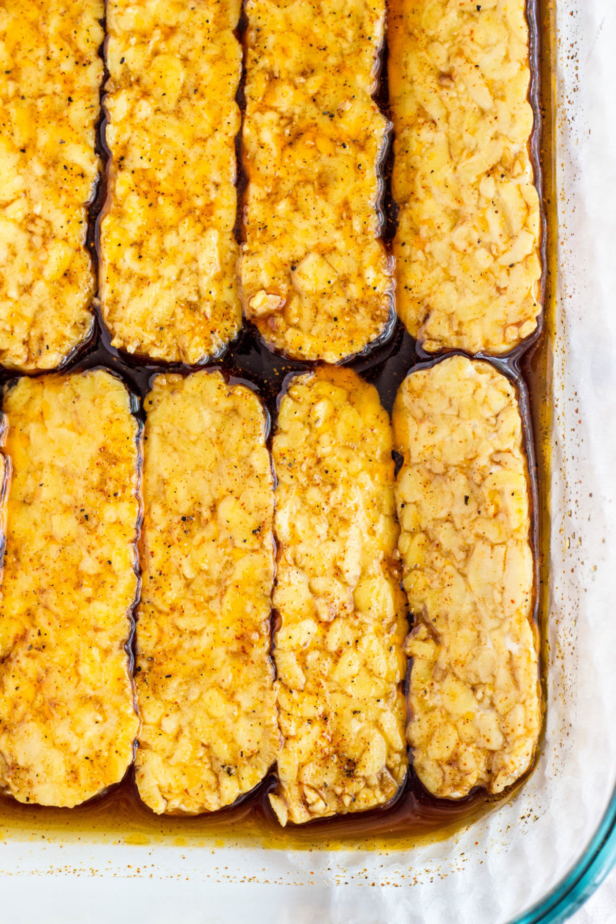 Close up of Tempeh slices is a glass dish with marinade. 