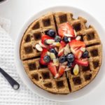 Top view of Cinnamon Rye Waffle topped with strawberry slices, blueberries and almond slivers on a white plate.