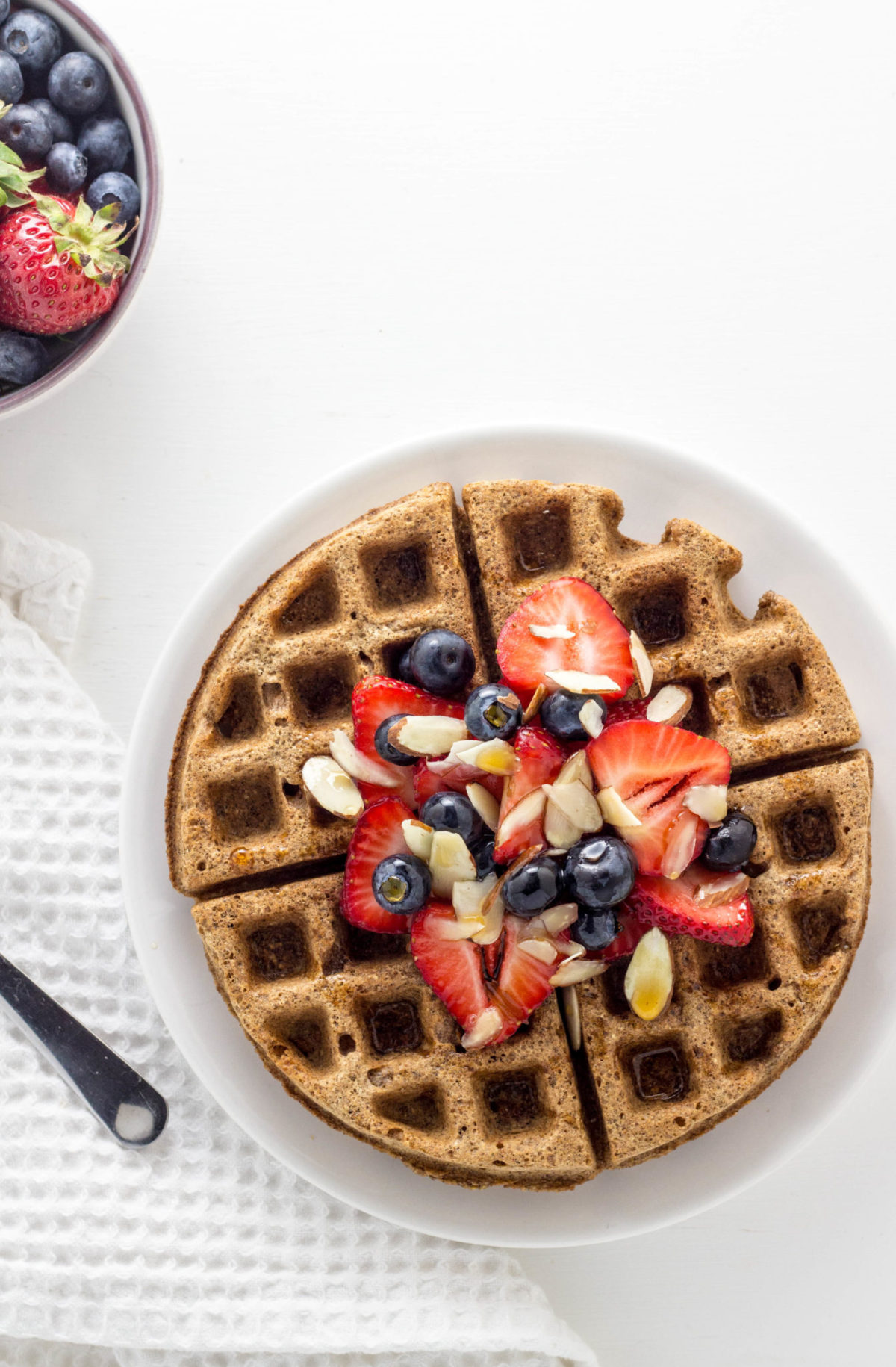 Overhead shot of Vegan Cinnamon Rye Waffles topped with strawberries, blueberries, almond slices and syrup.