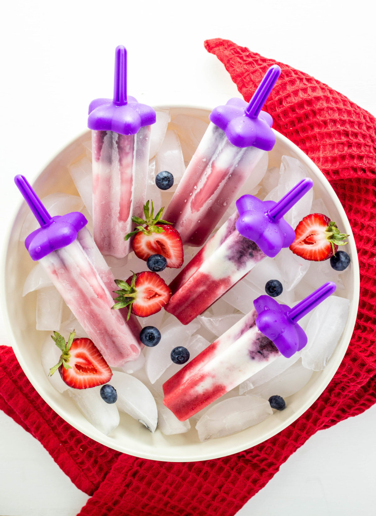 Top view of Vegan Red, White and Blue Popsicles in a large bowl with ice and berries. 