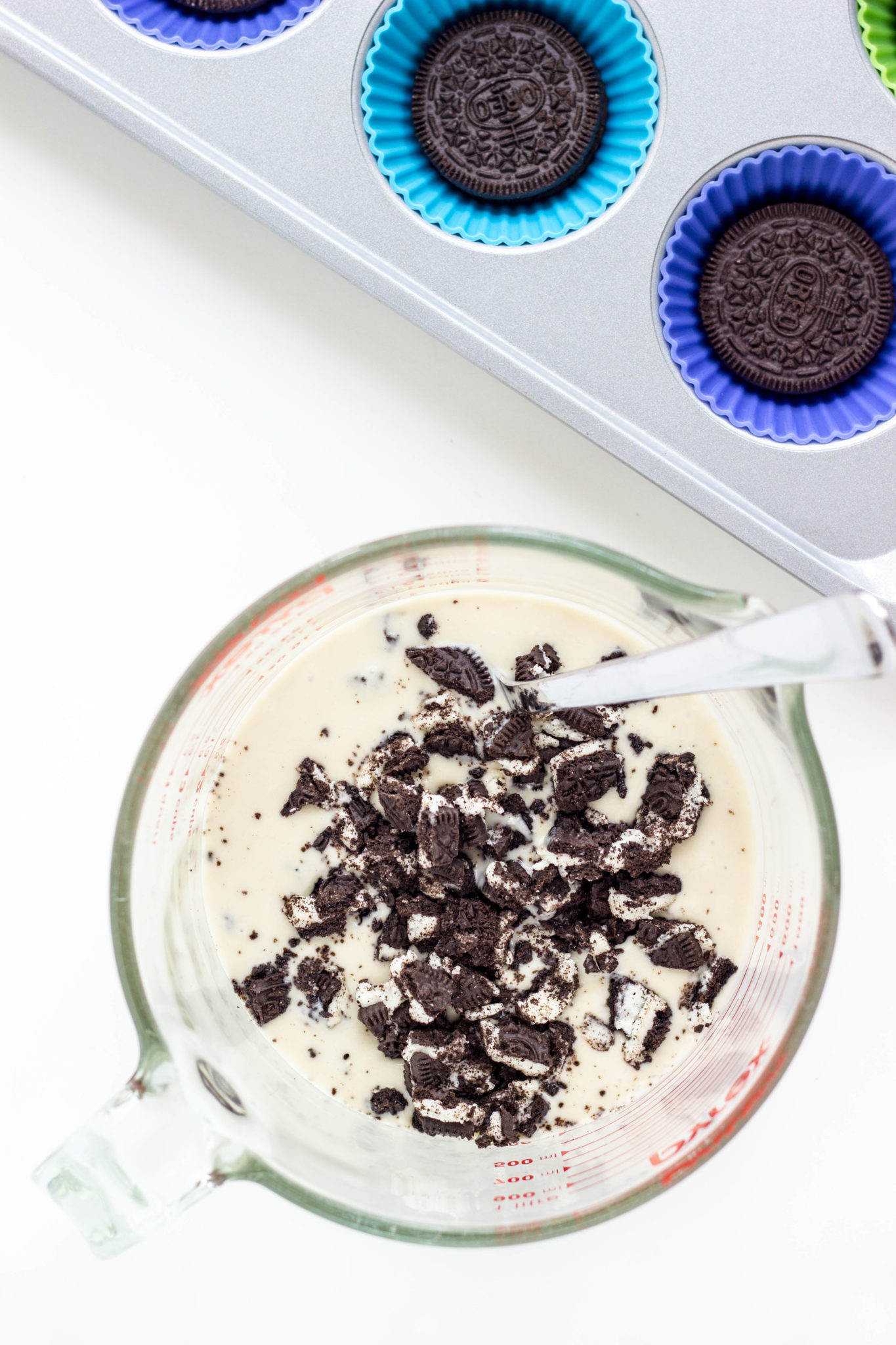 A large measuring cup of  ice cream base with crushed chocolate sandwich cookies. 