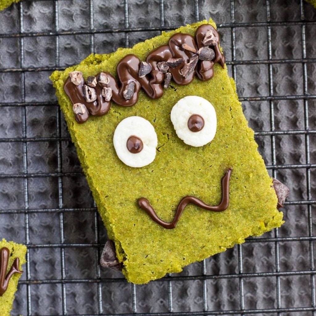 Close up Top view of Frankenstein Vegan Snack Cake. It's a green square cake decorated with melted chocolate, marshmallow and chocolate chips to look like a Frankenstein face.
