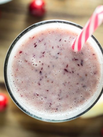 Top view of Cranberry Apple Smoothie with a straw on a wood background with cranberries and apple slices.