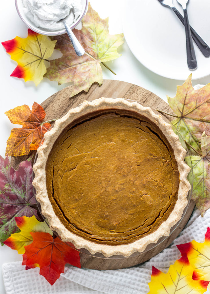 Top view of a whole Vegan Cardamom Pumpkin Pie with fall leaves scattered around. 