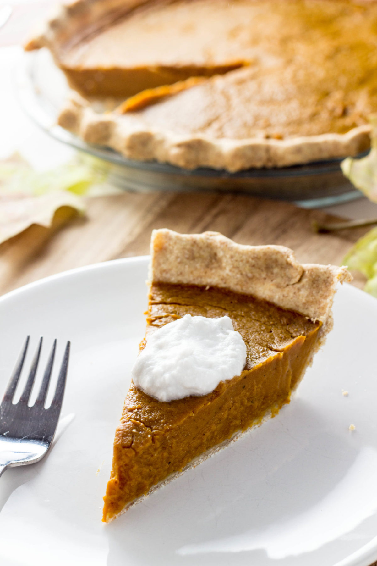 Side view of a slice of Vegan Cardamom Pumpkin Pie on a white plate with a fork to the side. 