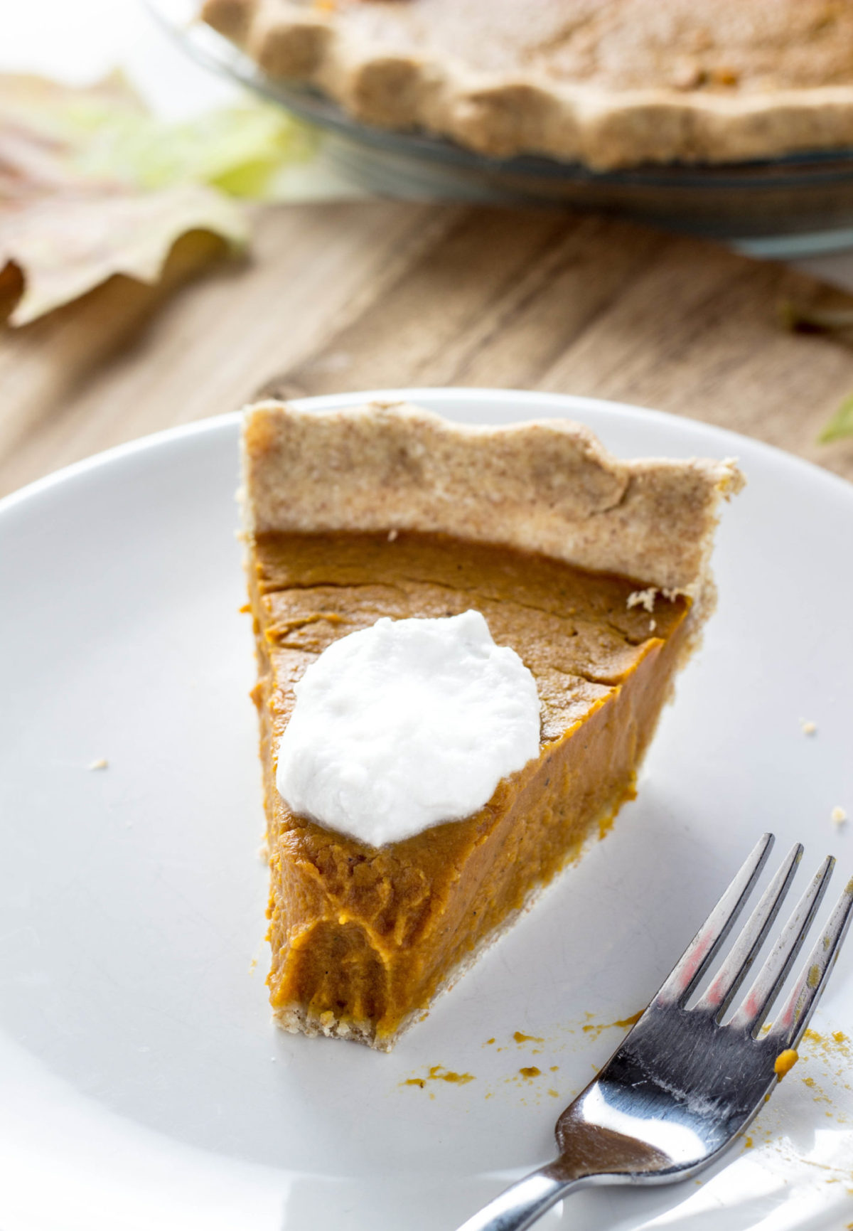 Slice of Vegan Cardamom Pumpkin Pie on a white plate with a dallop of non dairy whipped cream on top. 