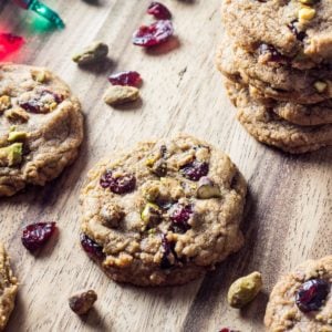Vegan Cranberry Pistachio Cookies on a wood background with dried cranberries and pistachios scattered around.