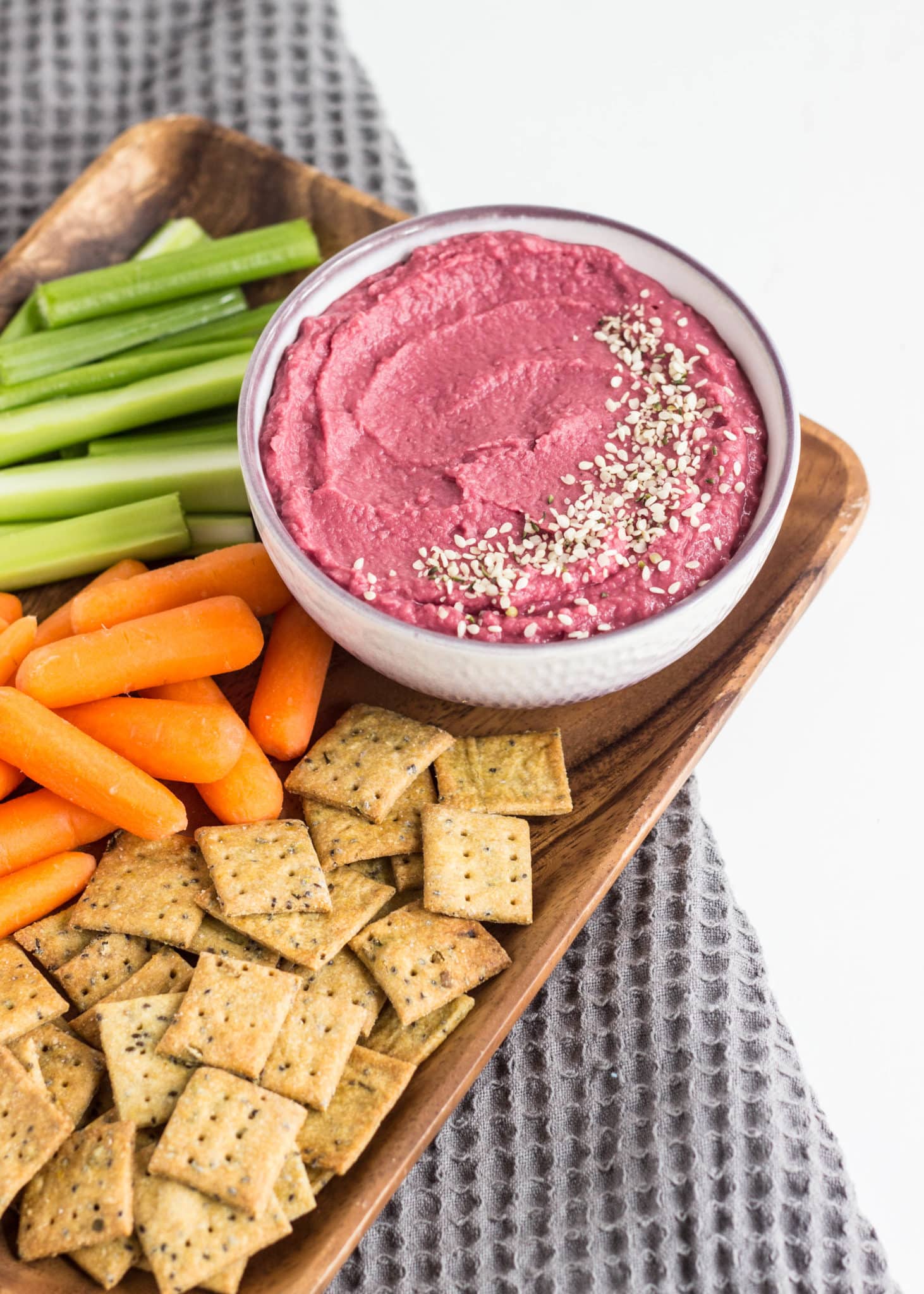 5 Minute Vegan Beetroot Bean Dip on a wooden platter with carrots, celery and crackers.