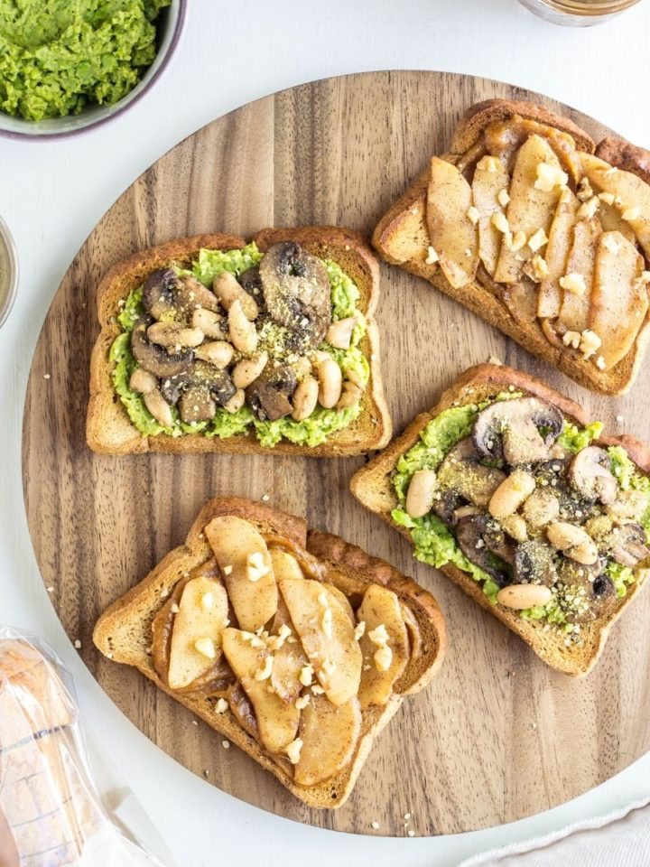 Top view of four slices of Gluten Free Vegan Toast on a round wooden board with bowls of toppings surrounding.