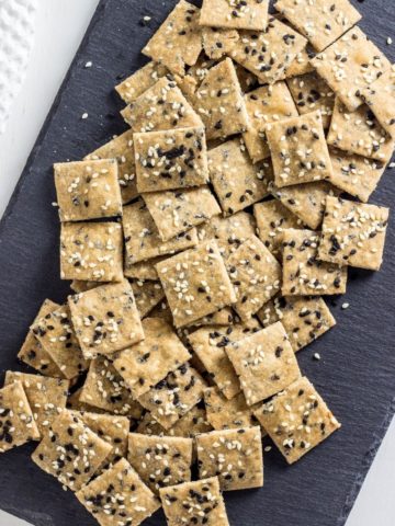 Top view of Sesame Seed Olive Oil Crackers on a slate cutting board with a white background.
