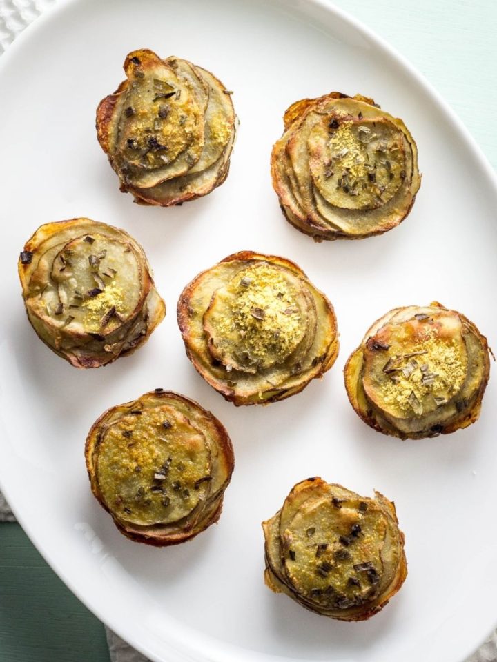 Top view of several Vegan Cheesy Potato Stacks on a white serving plate with a light mint colored background.
