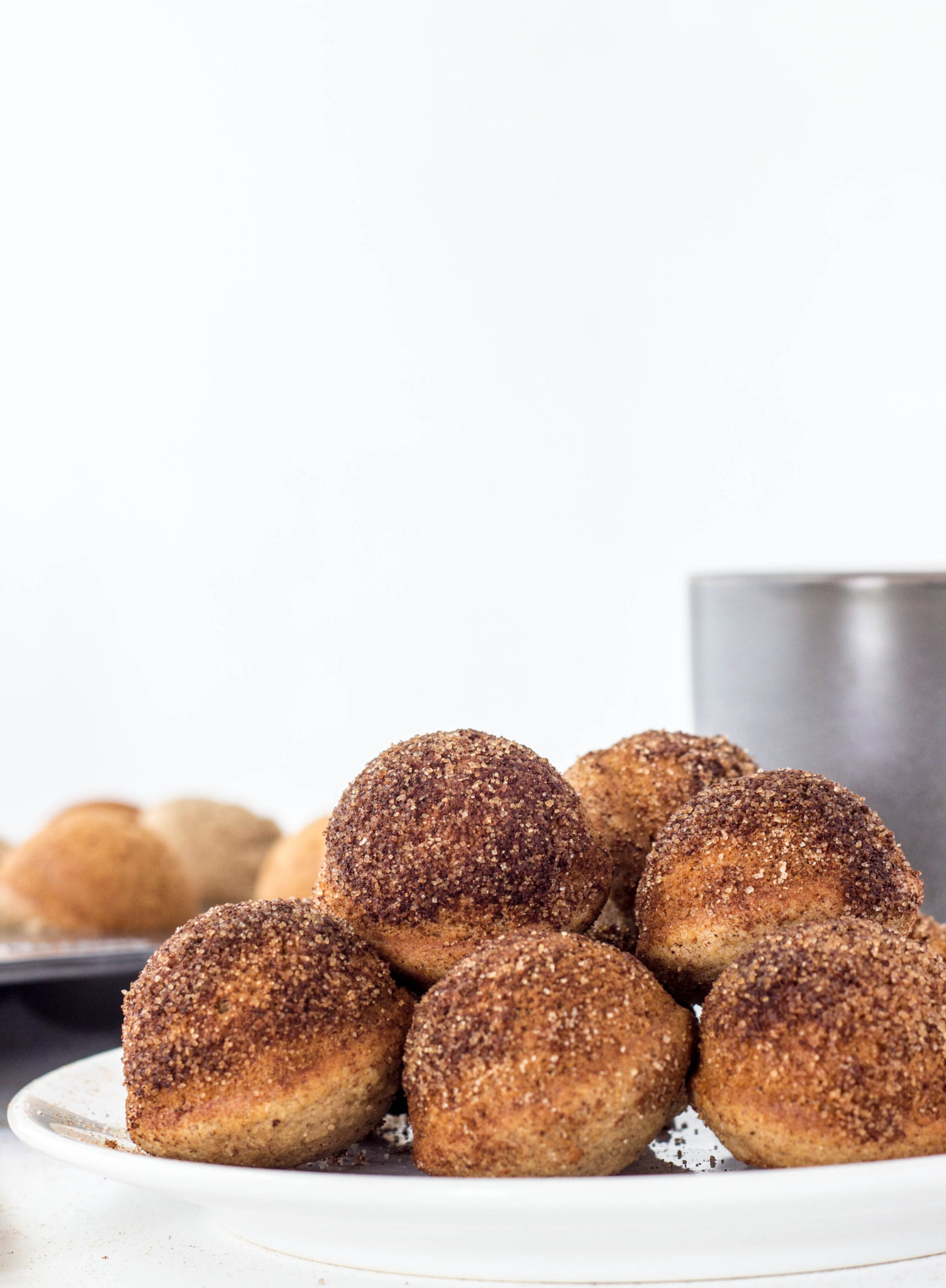 Side view of several Baked Cinnamon Sugar Doughnut Holes on white plate. 