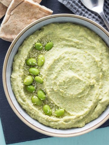 Top View of Vegan Edamame Hummus in a bowl with whole edamame scattered on top and pita wedges on the side.