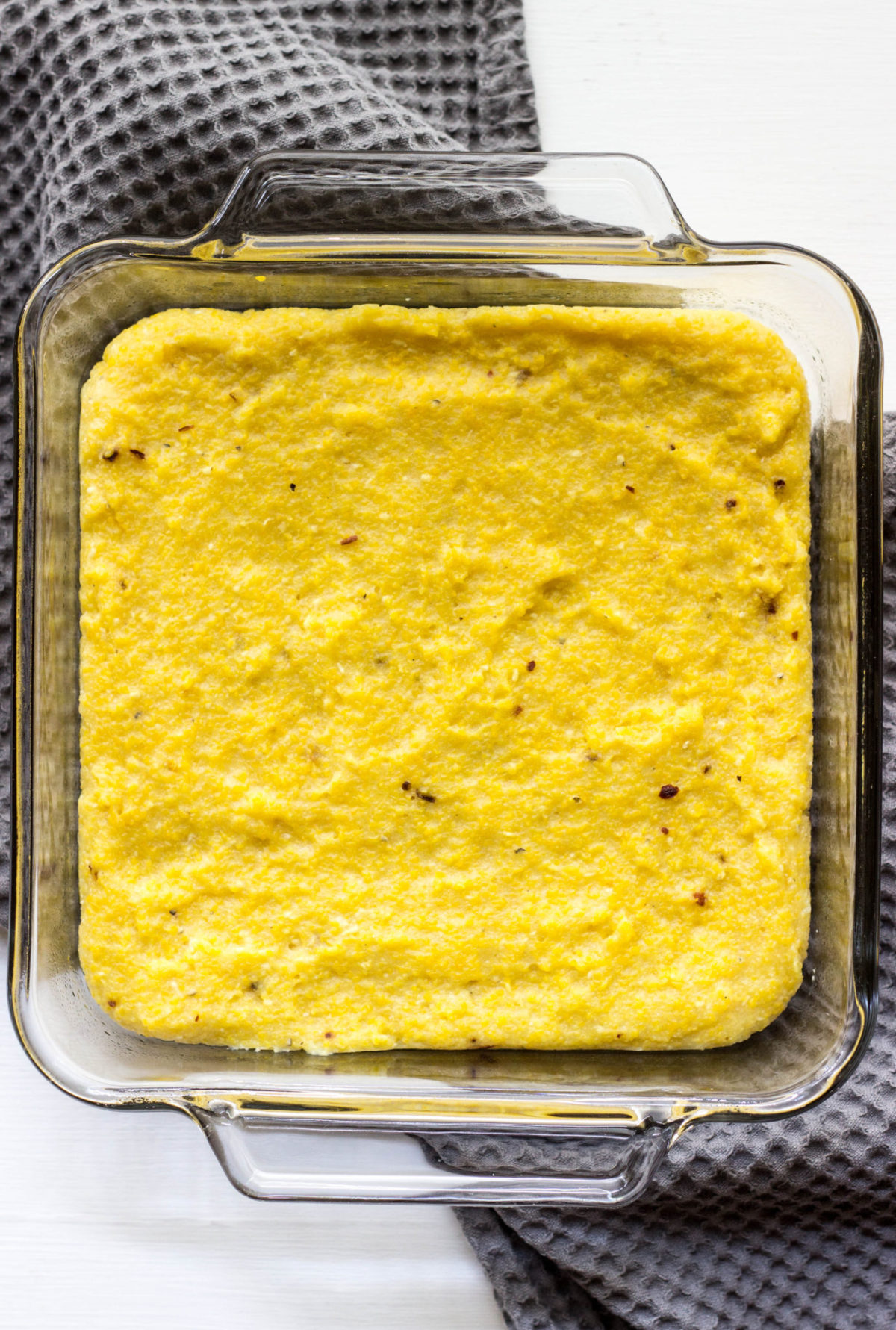 Polenta in a square baking dish sitting on a gray towel. 