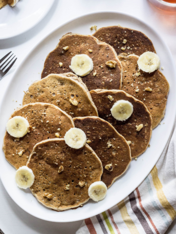 Top view of Whole Wheat Banana Nut Pancakes on a white serving plate with banana slices.