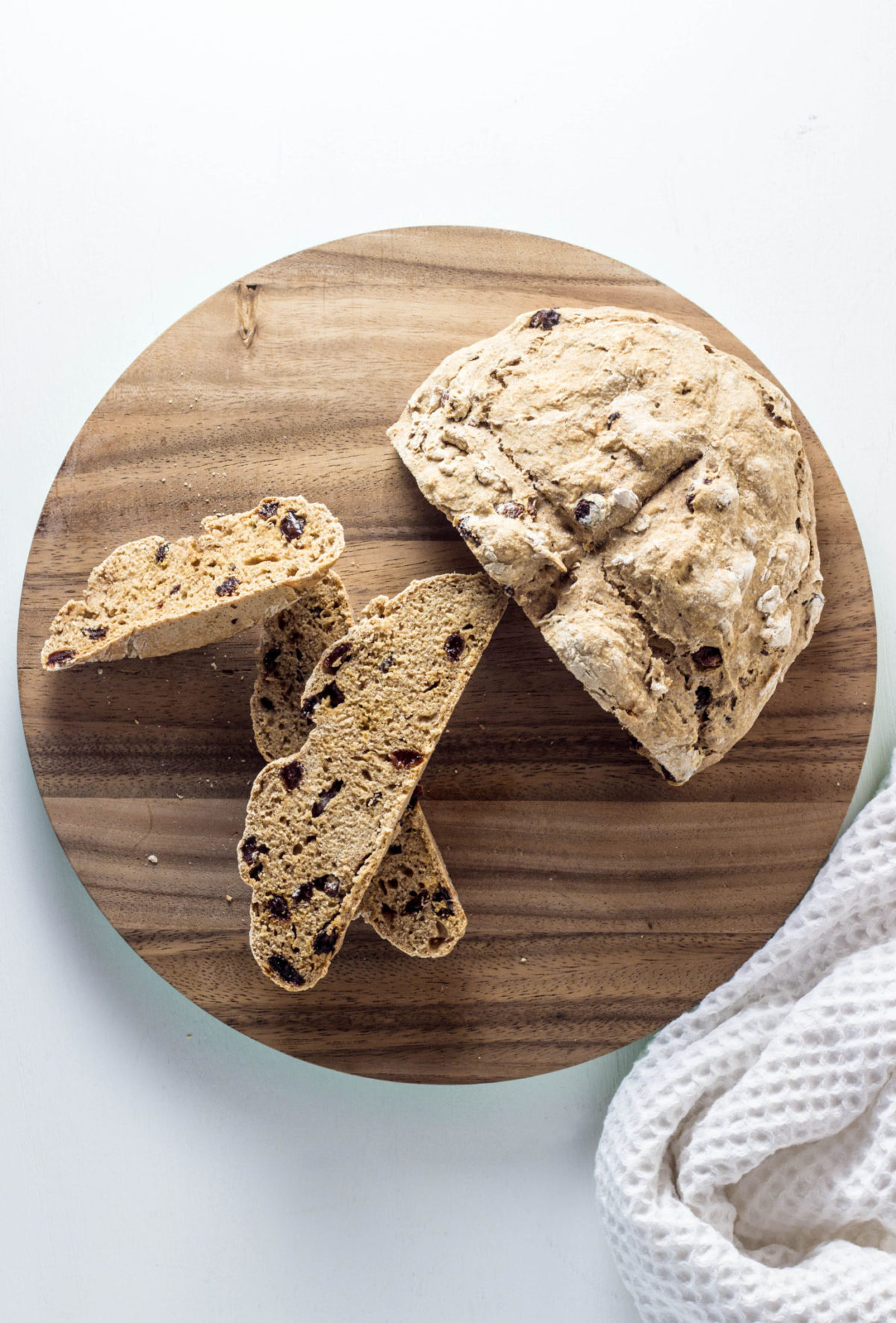 Top view of a loaf of soda bread with three slices on a round wooden cutting board against a white background. 