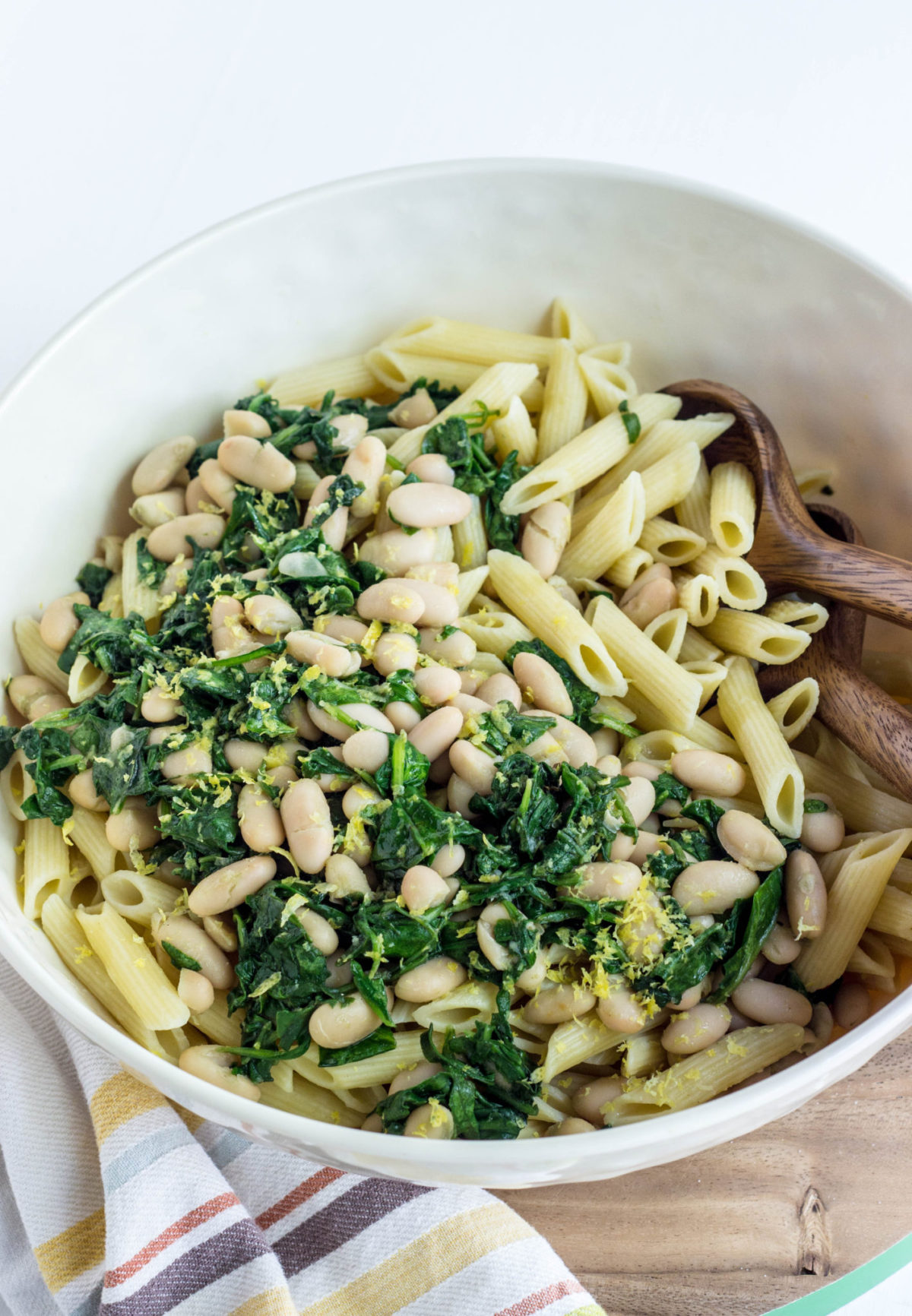 Top view of a bowl of pasta topped with white beans, sautéed spinach and lemon zest. 