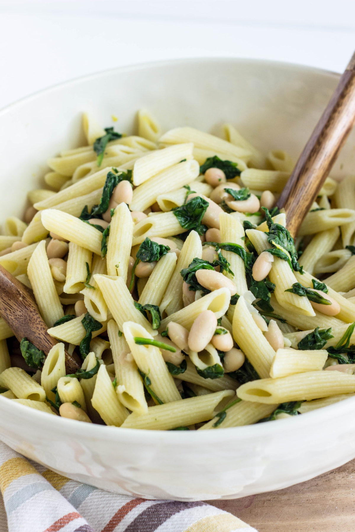 Close up image of pasta tossed with white beans and sautéed spinach. 