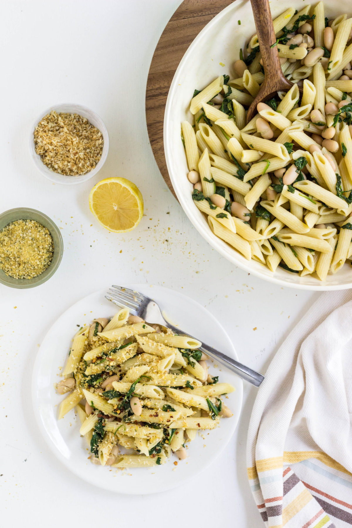 Overhead view of a plate of White Beans and Greens Pasta with a large bowl of pasta to the side. 